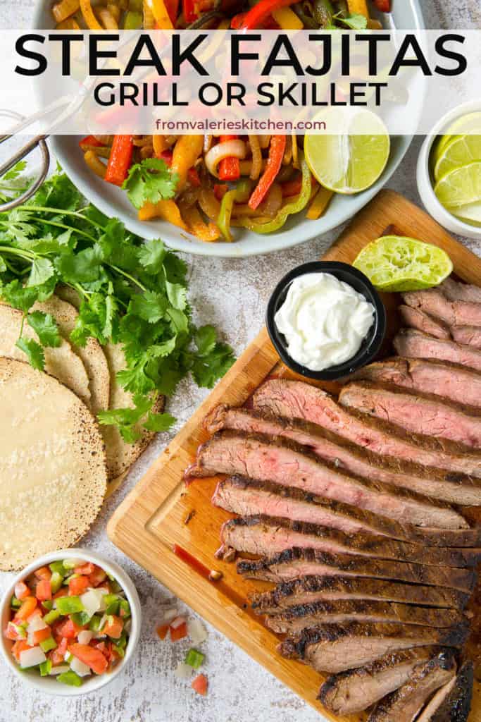 Sliced steak on a cutting board and a bowl of sliced bell peppers and onions.