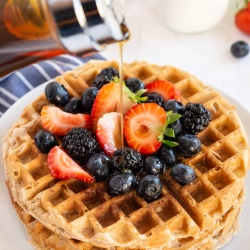 Maple syrup pours down on to a stack of waffles with fresh berries.