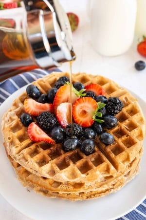 Maple syrup pours down on to a stack of waffles with fresh berries.