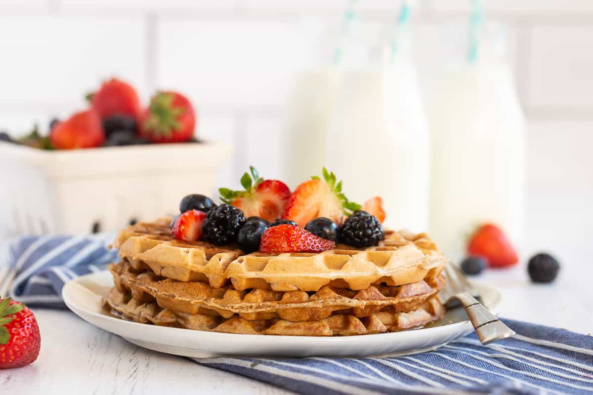 A stack of waffles on a white plate topped with fresh berries.