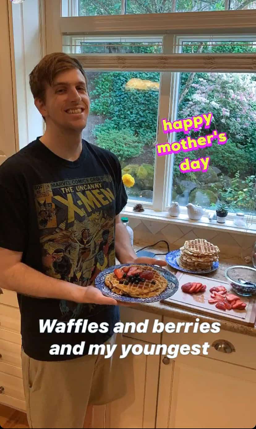 A young man holding a plate of waffles in a kitchen.