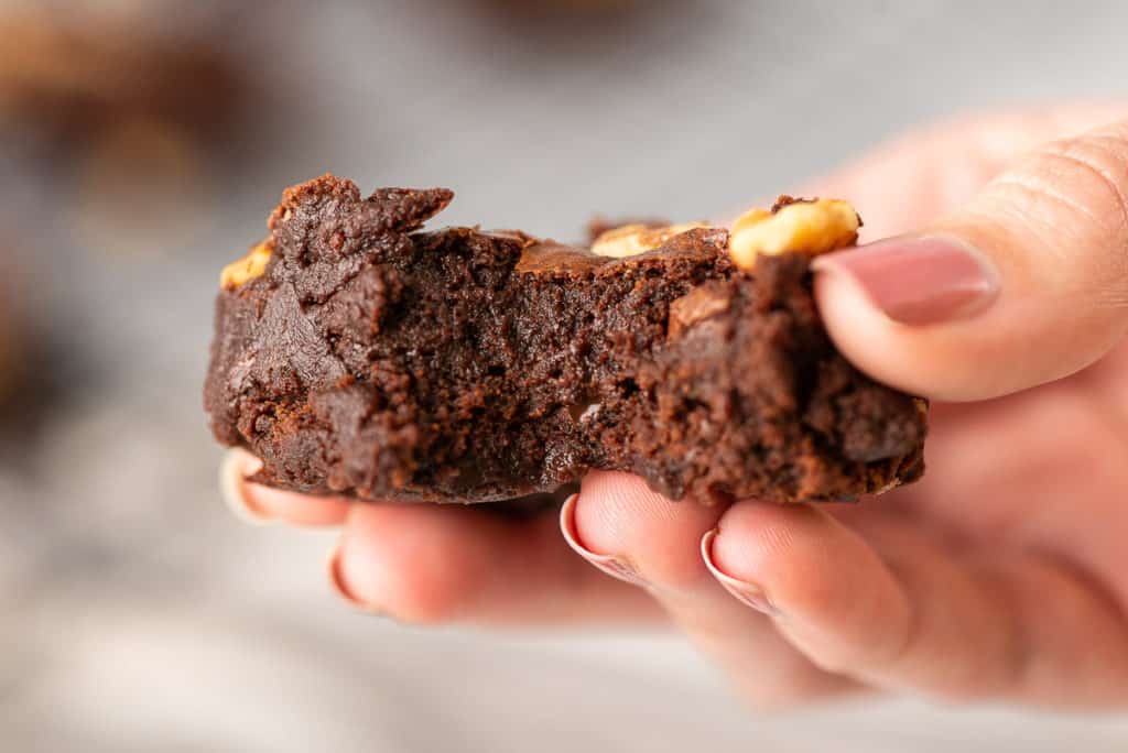 A hand holding a brownie with a bite missing.
