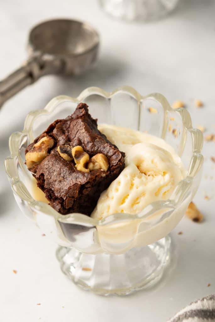 A glass dish filled with vanilla ice cream and a brownie.