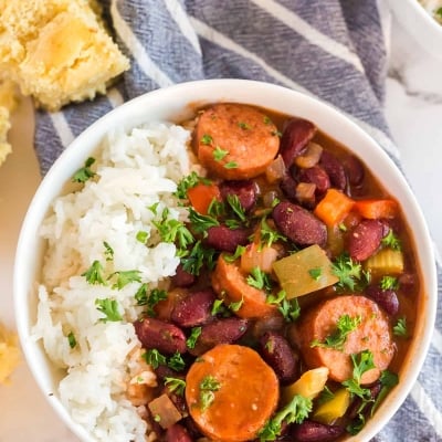 A white bowl filled with red beans sausage and rice on a blue and white cloth.