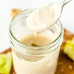 Caesar salad dressing drips from a spoon into a mason jar.