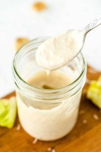 Caesar salad dressing drips from a spoon into a mason jar.