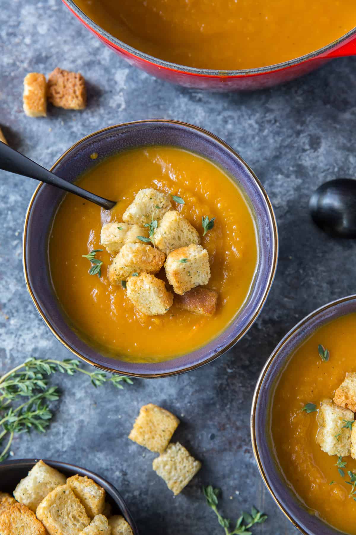 A blue bowl filled with Butternut Squash Soup topped with croutons.
