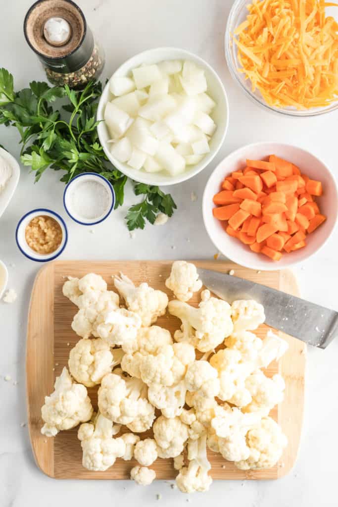 Cauliflower florets on a cutting board surrounded by other ingredients.