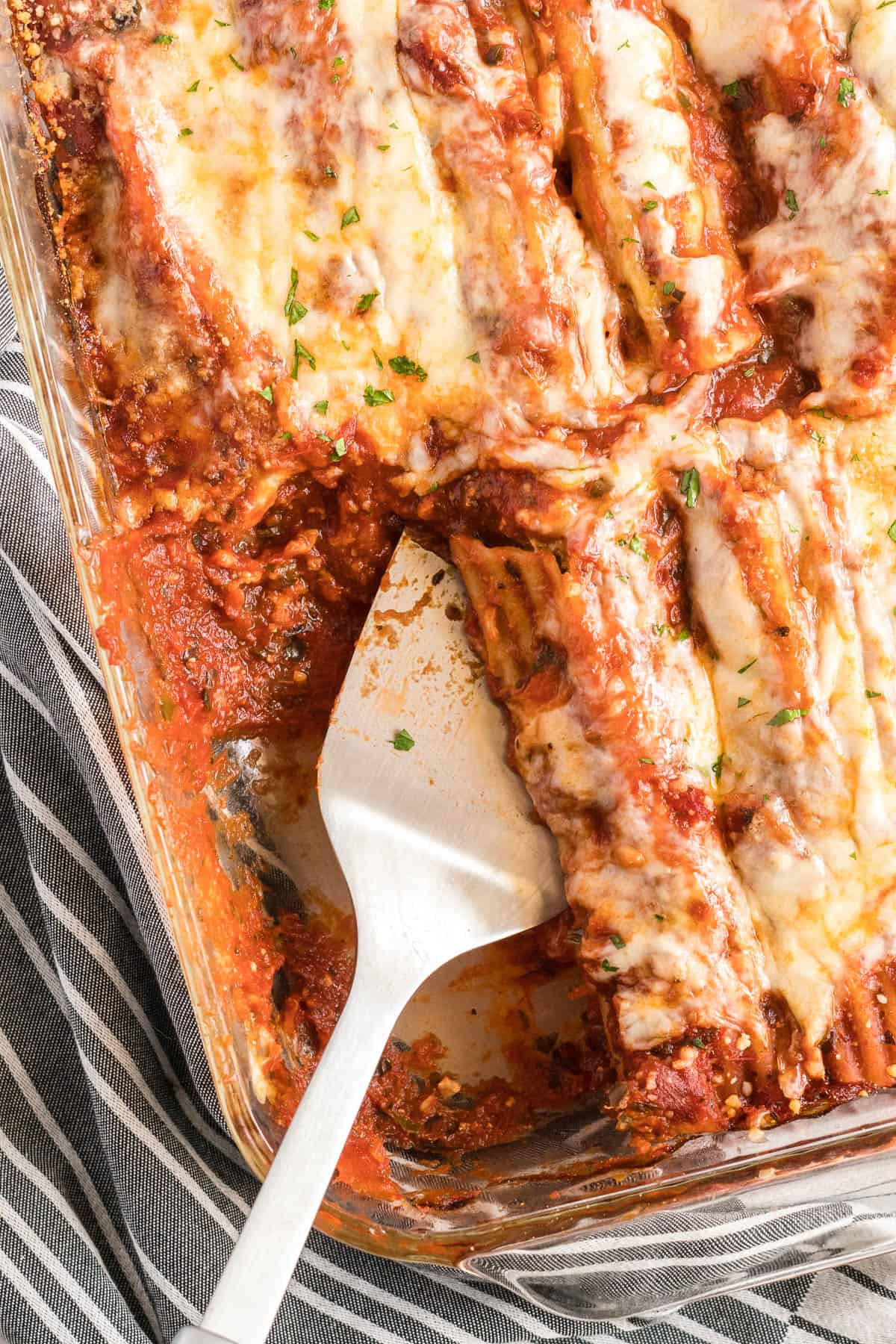 A spatula scoops manicotti from a baking dish.