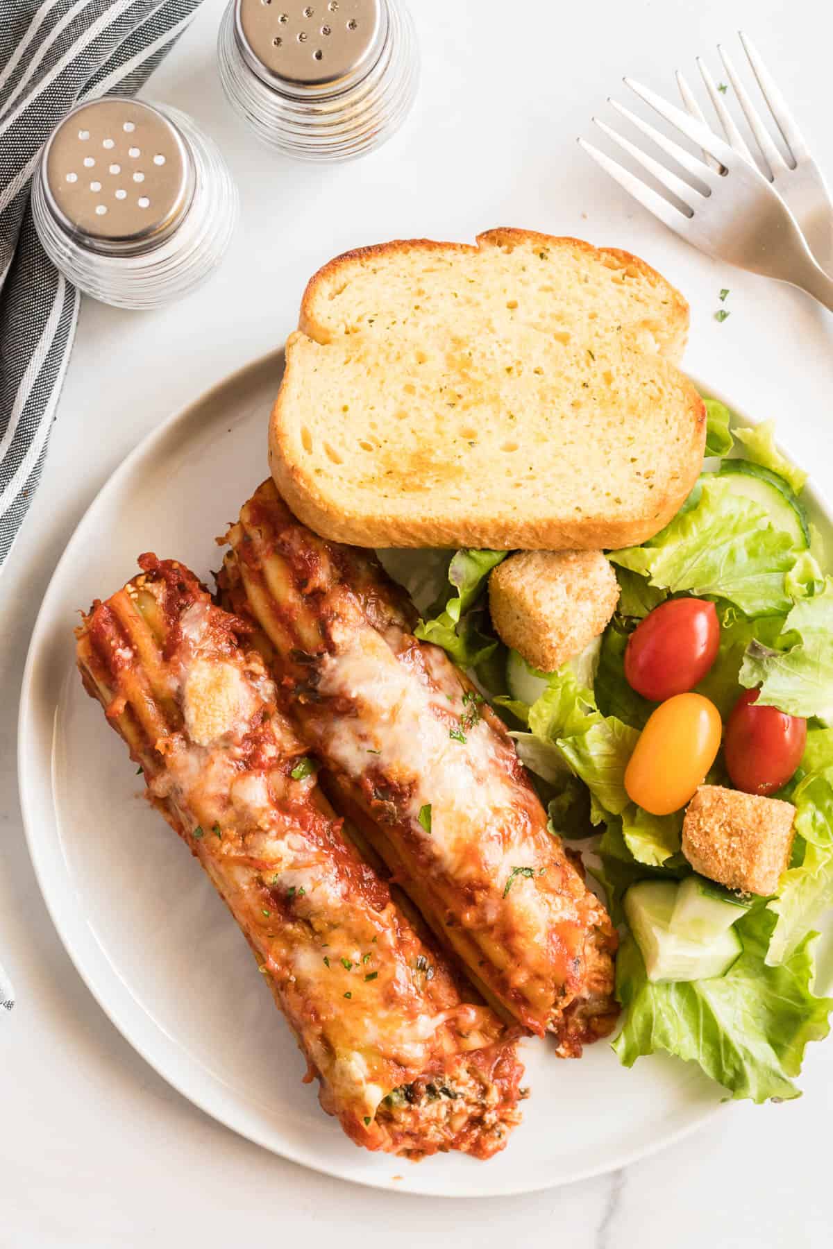 Manicotti, salad and toast on a white plate.