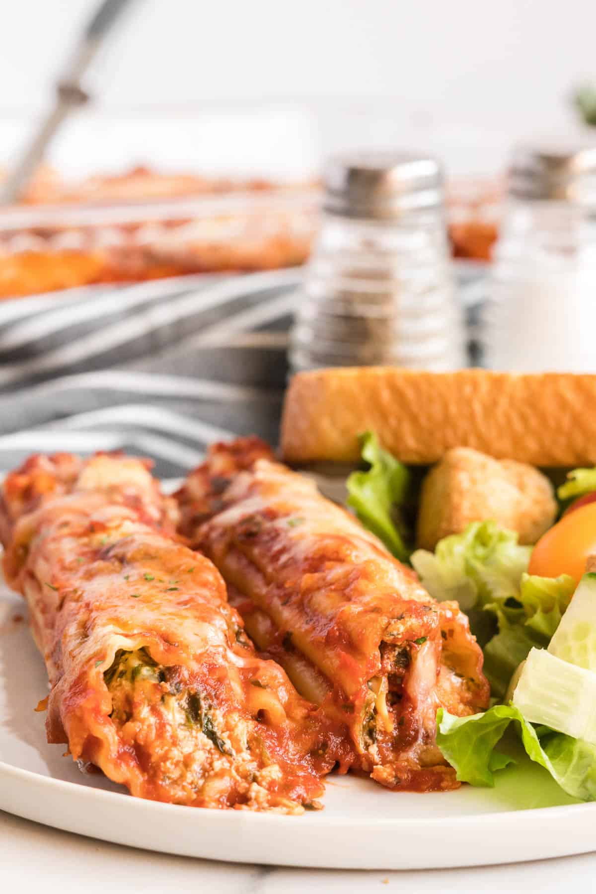 Manicotti and salad on a white plate.