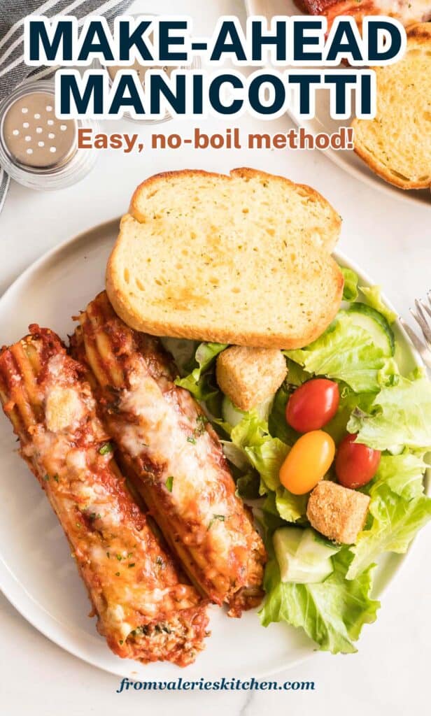 A top down shot of manicotti on a white plate with toast and green salad.