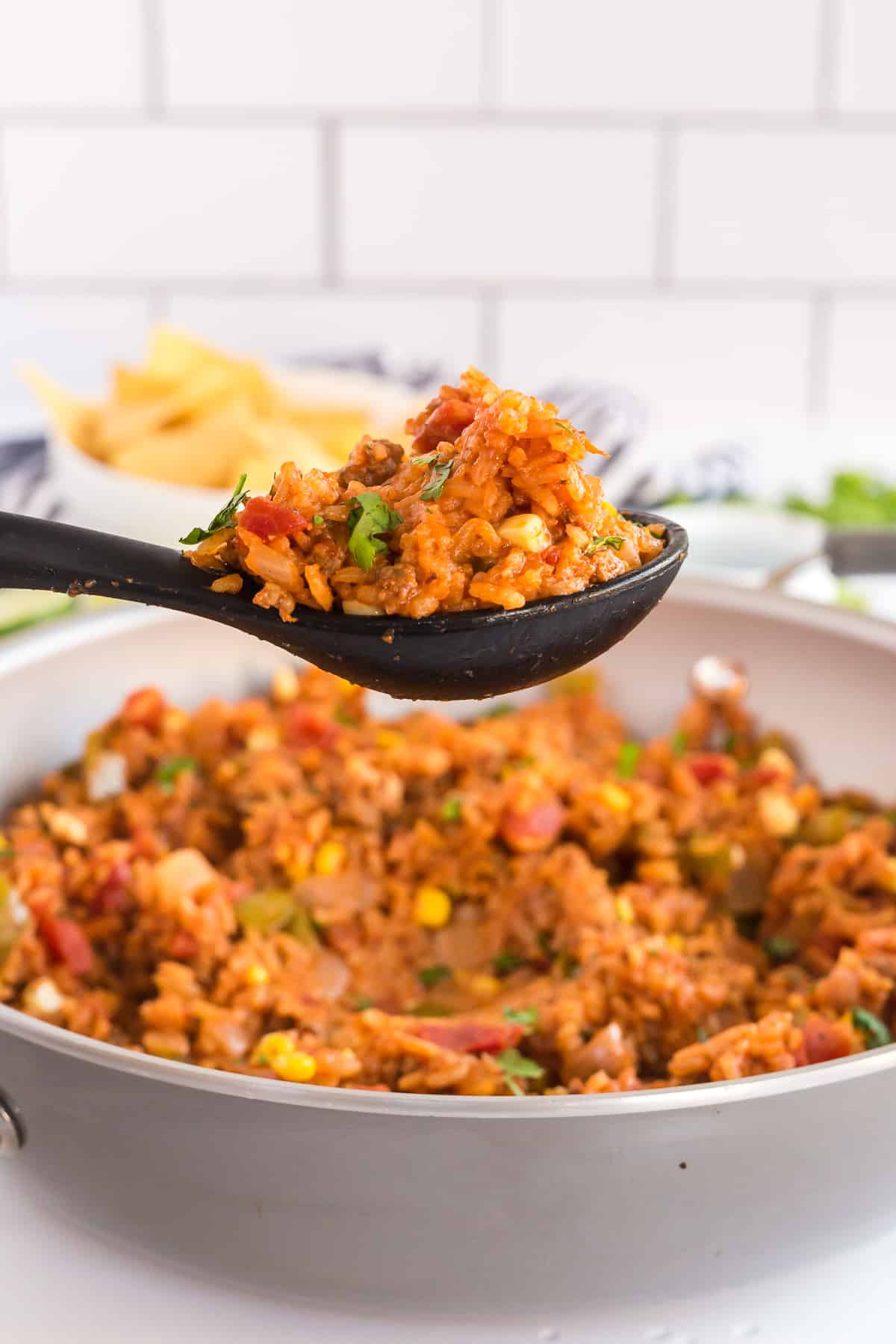 A spoon scoops Spanish Rice from a skillet.