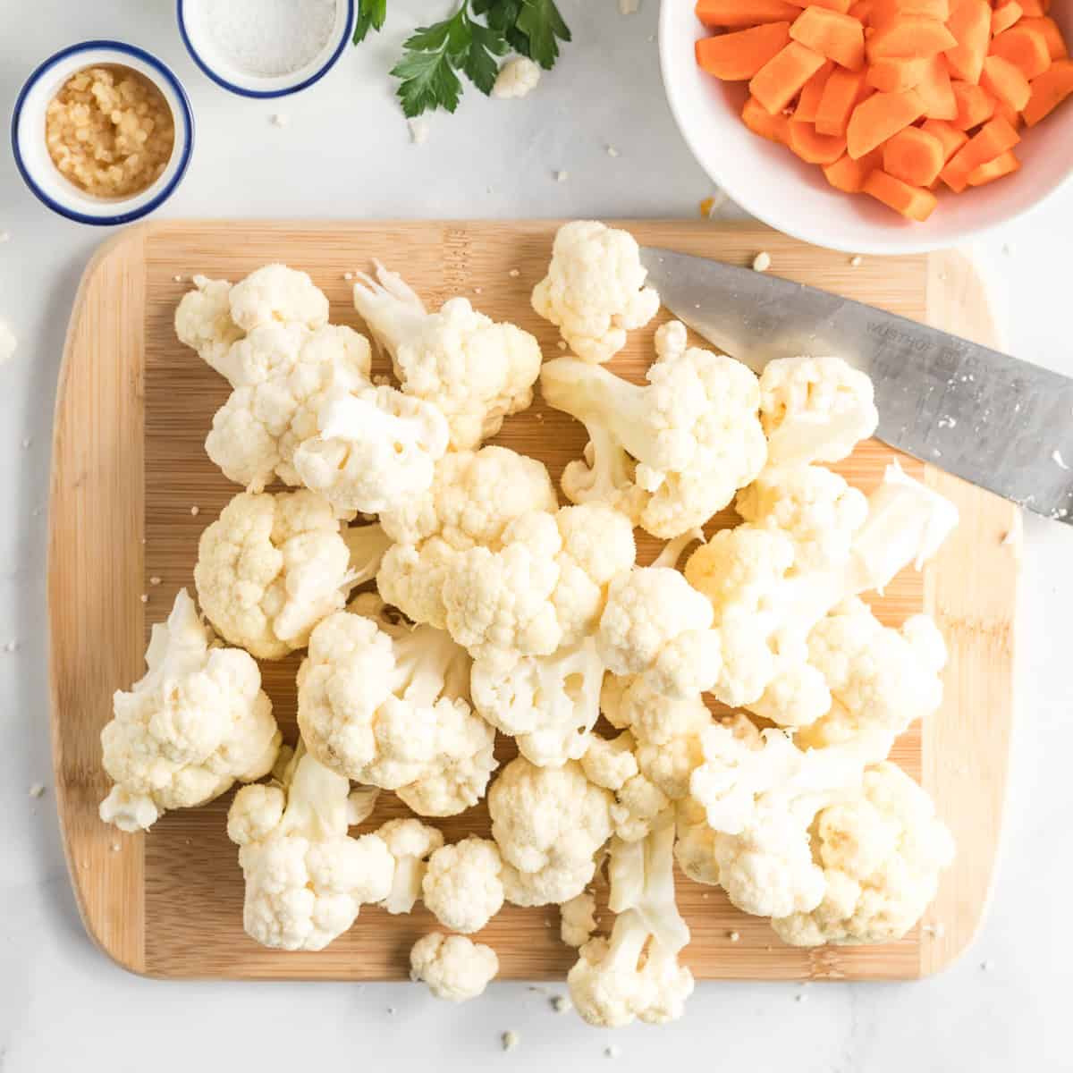 Cauliflower florets on a cutting board surrounded by other ingredients.