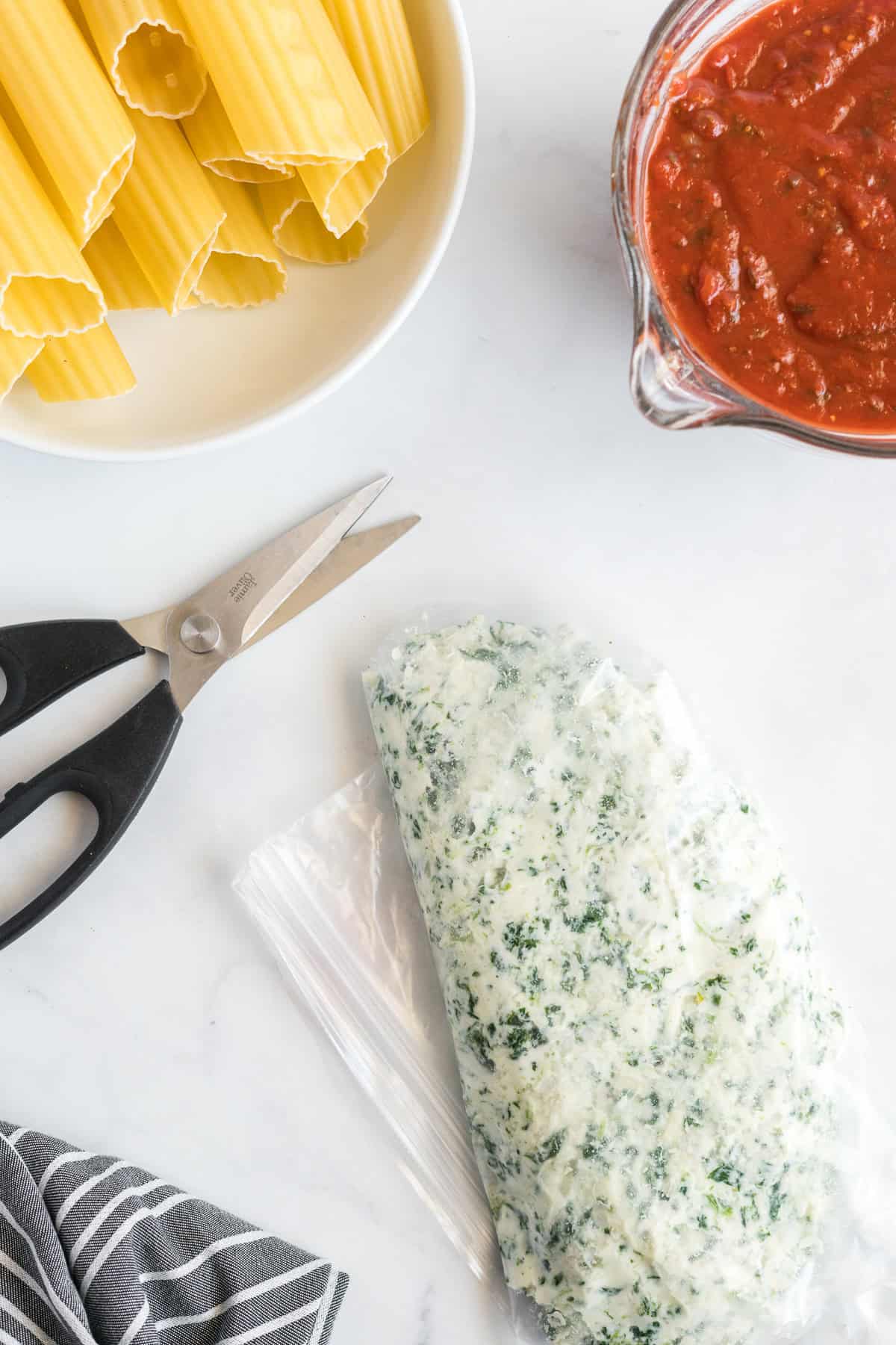 Cheese and spinach manicotti filling in a plastic bag next to a pair of scissors.