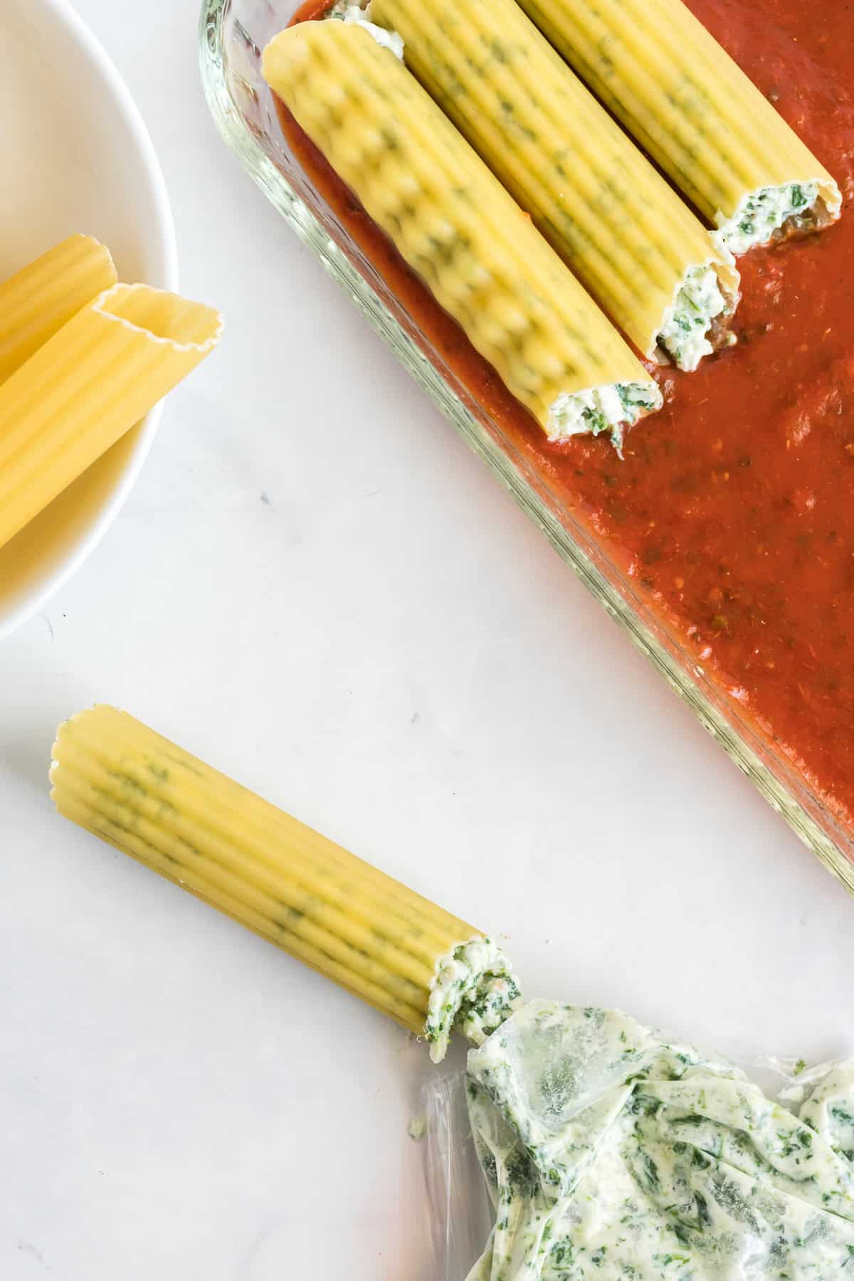 A plastic bag pushing filling into a manicotti noodle.