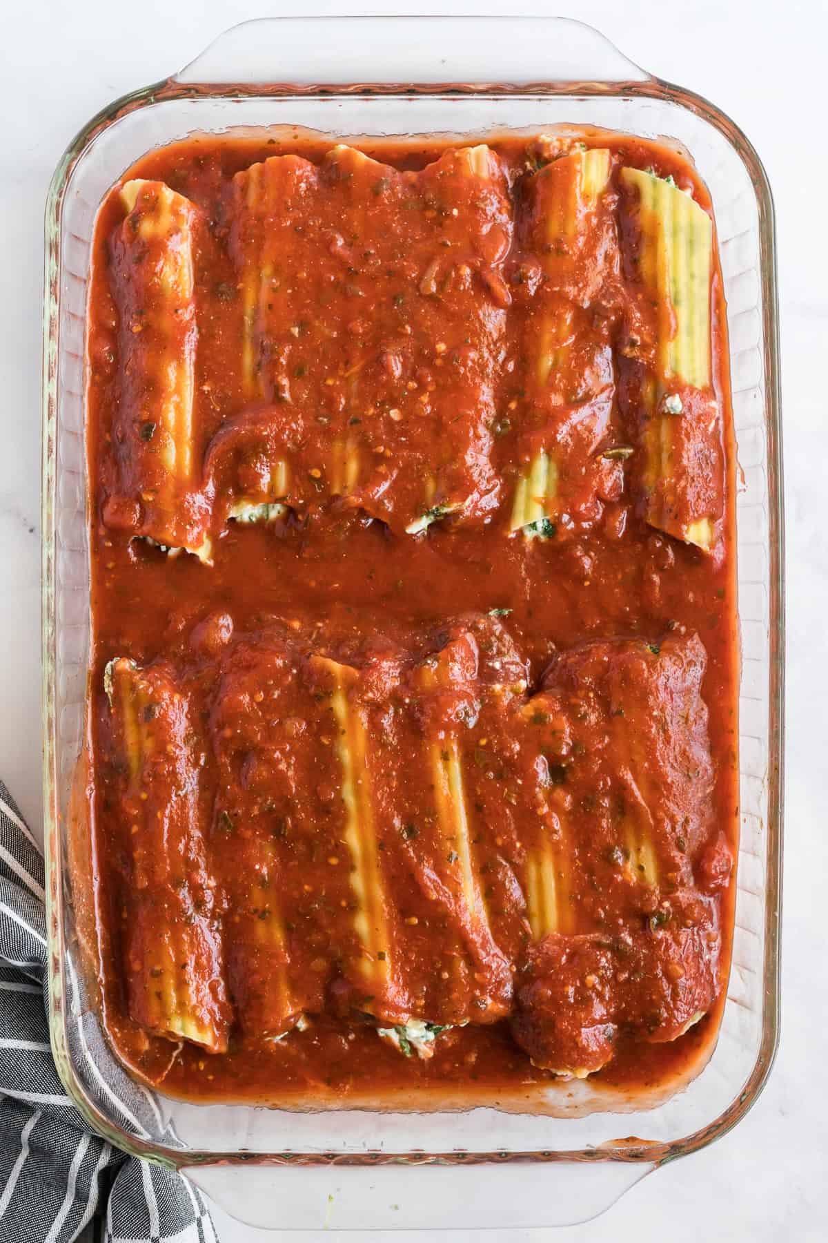 Stuffed manicotti in a baking dish topped with marinara sauce.