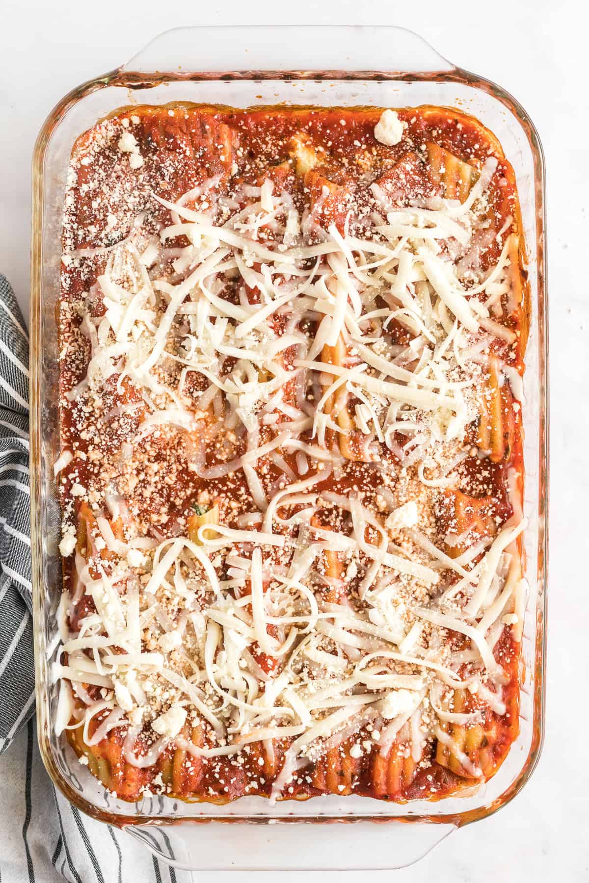 A baking dish full of manicotti topped with marinara sauce and shredded cheese.