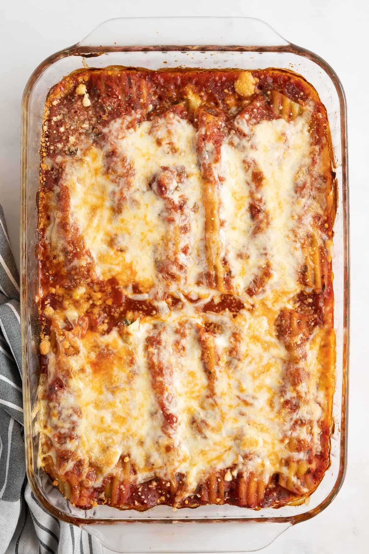 Manicott in a baking dish topped with marinara sauce and melted cheese.