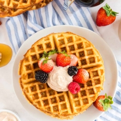 An over the top shot of waffles topped with berries and butter.