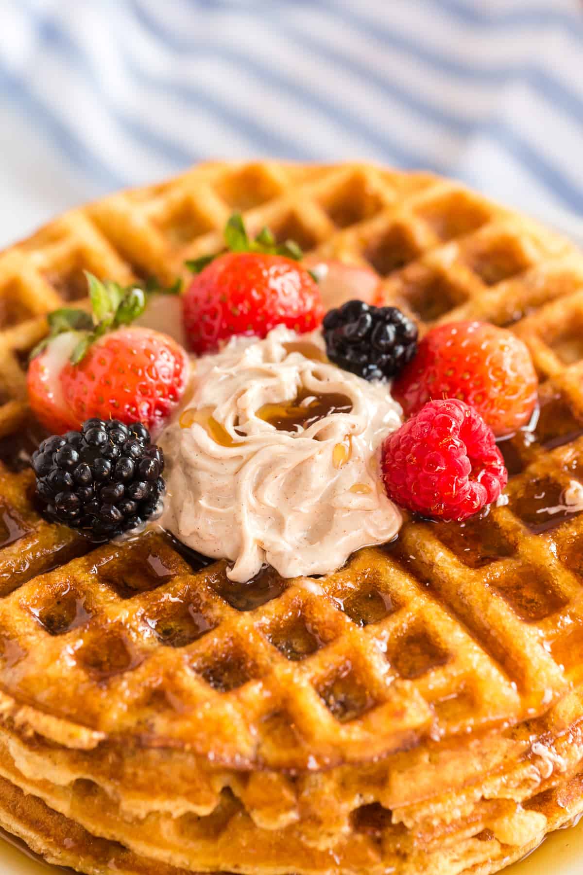 A closeup of a stack of cornbread waffles with berries and butter on top.