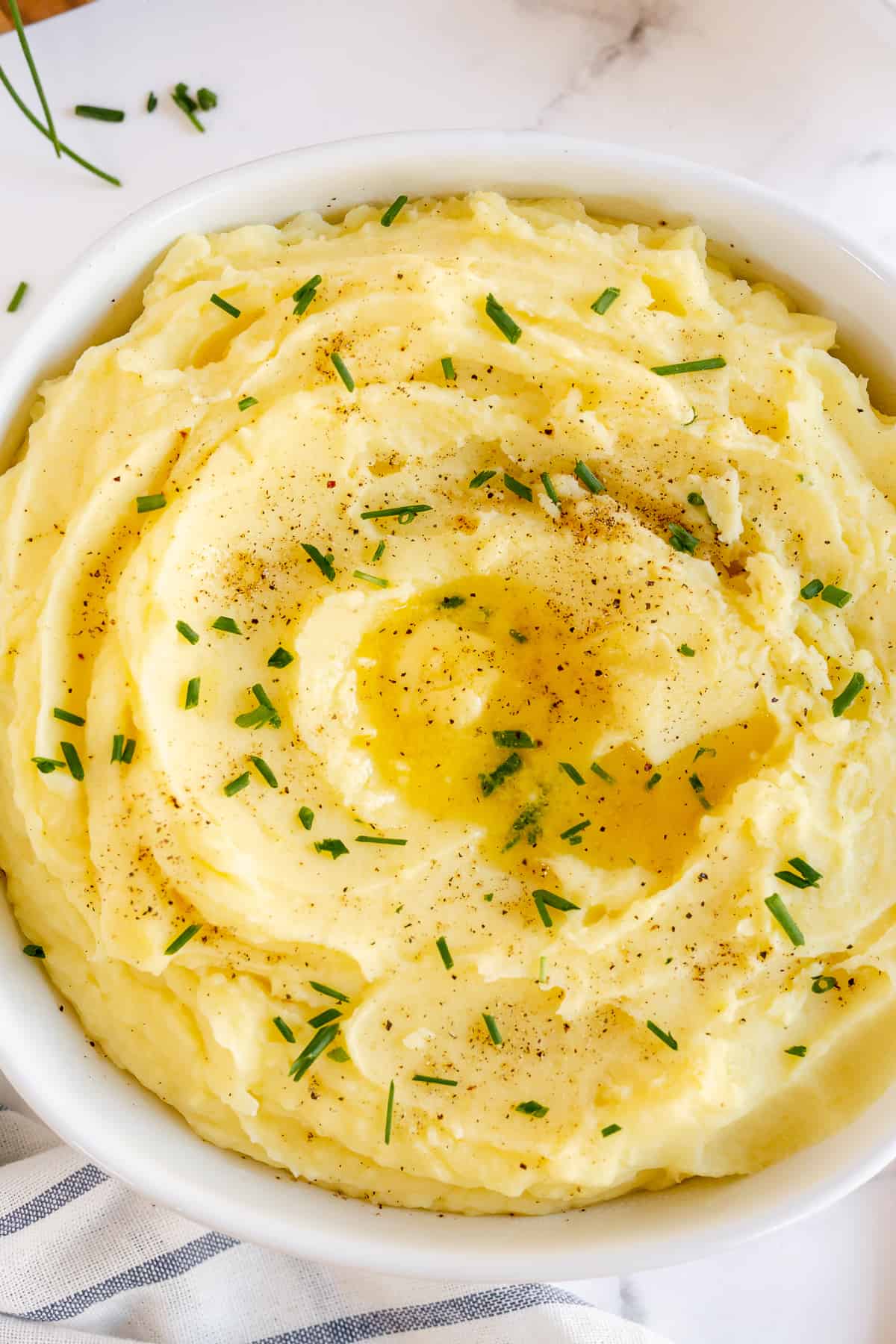 Mashed potatoes in a white bowl topped with butter and chives