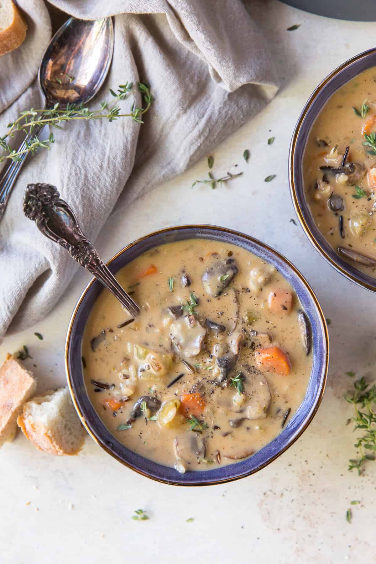 Two bowls of soup next to a cloth and pieces of bread.