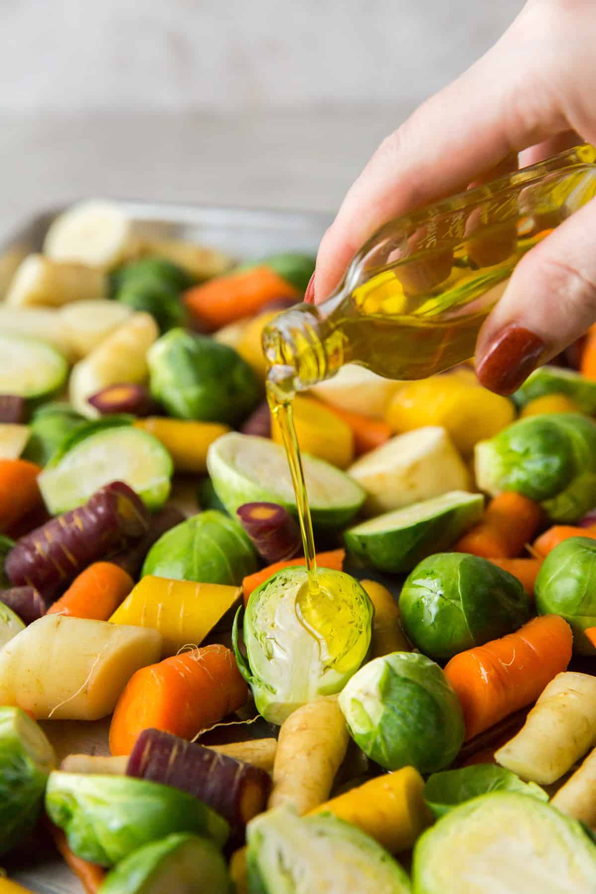 Oil is poured on to vegetables on a baking sheet.