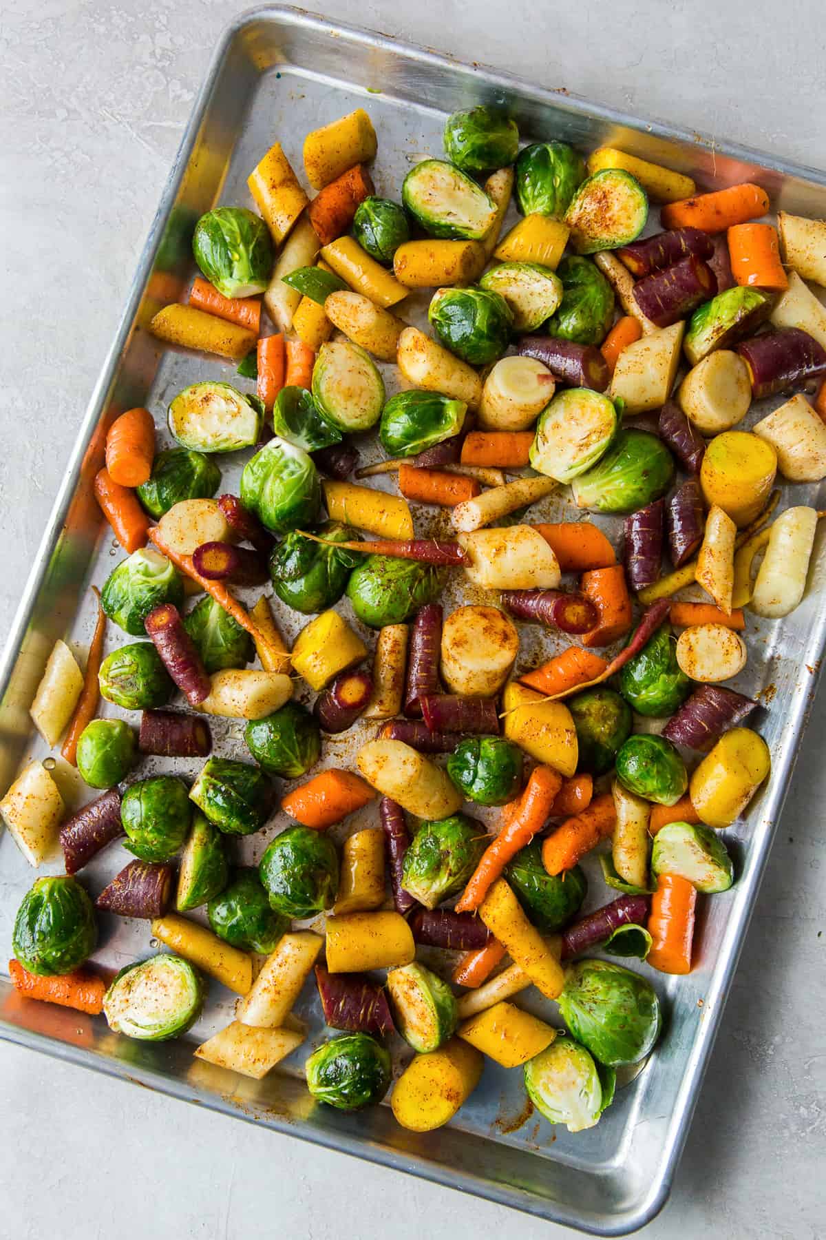 Rainbow carrots and Brussels sprouts with seasoning on a baking sheet.