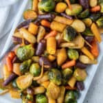 Roasted rainbow carrots and Brussels sprouts on a white platter.