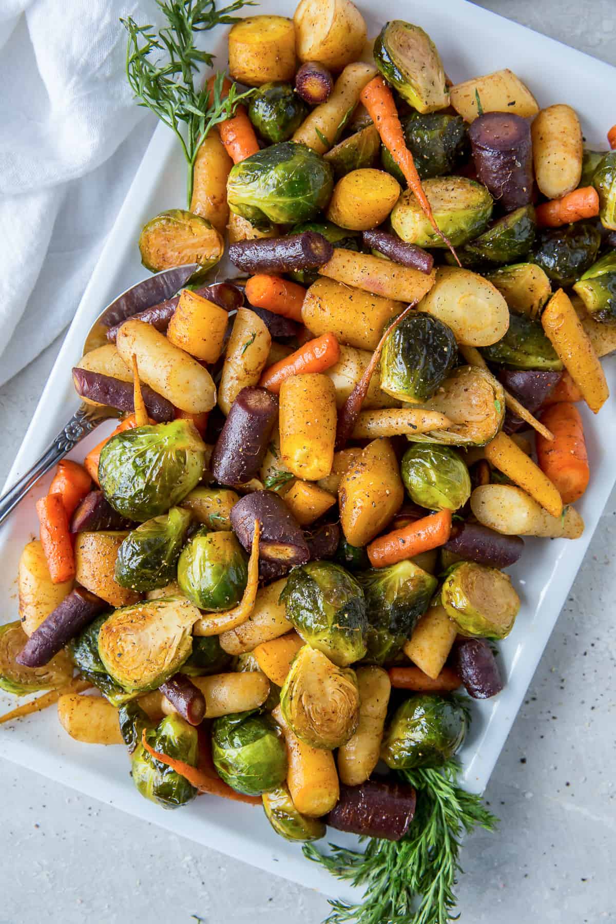 Roasted rainbow carrots and Brussels sprouts on a white platter.