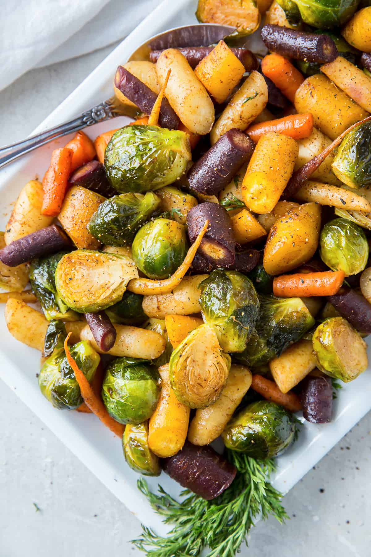 Roasted rainbow carrots and Brussels sprouts on a white platter.