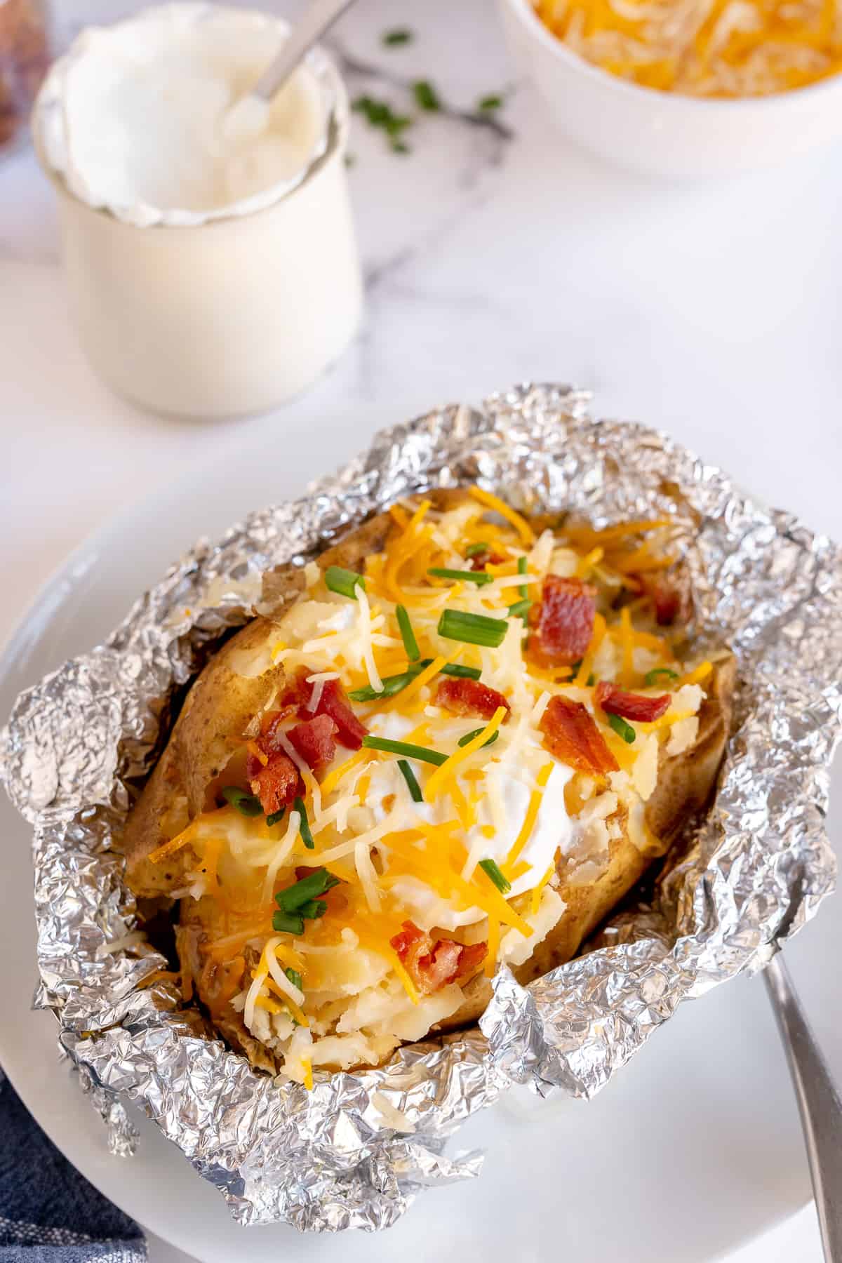 A baked potato with sour cream, cheese, and bacon on top of a sheet of foil.
