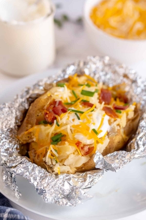 A baked potato topped with cheese, sour cream, and bacon on top of foil.