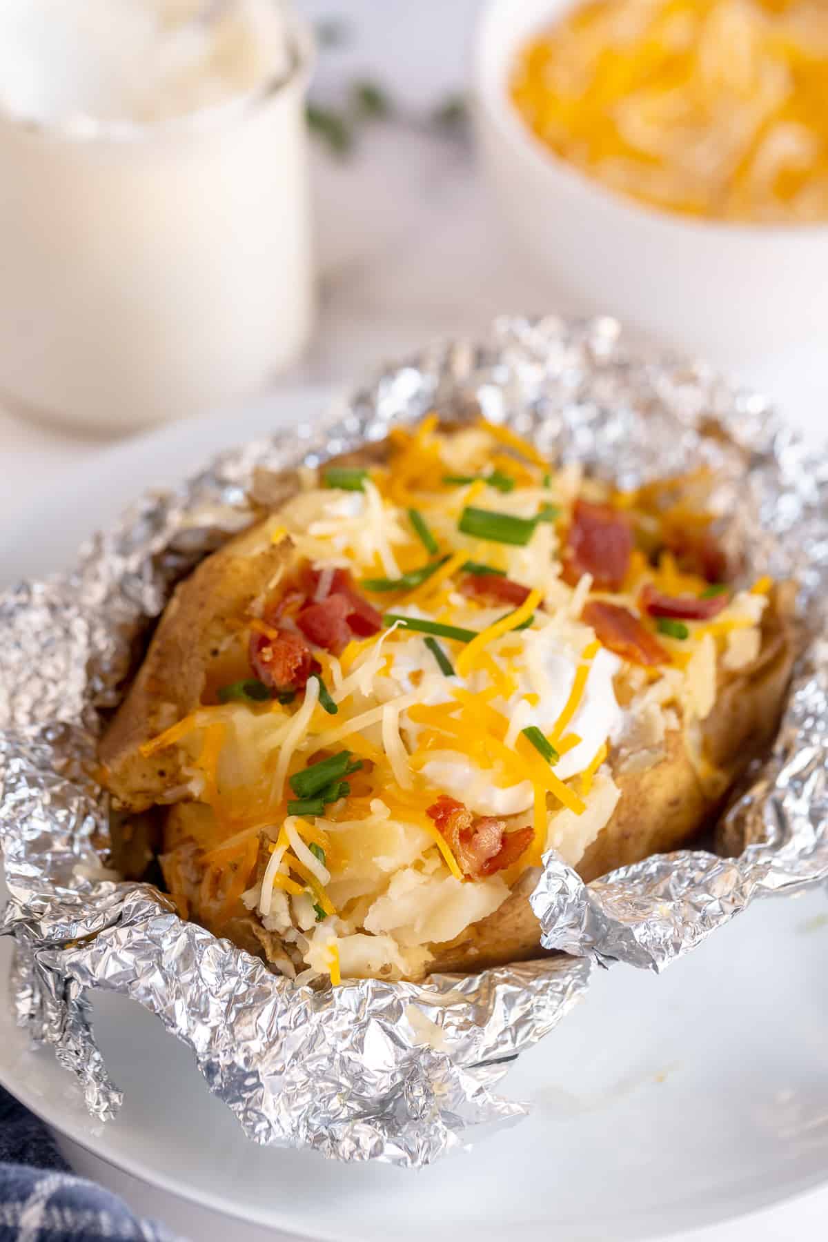 A Crock Pot Baked Potato topped with cheese, sour cream, and bacon on top of foil.