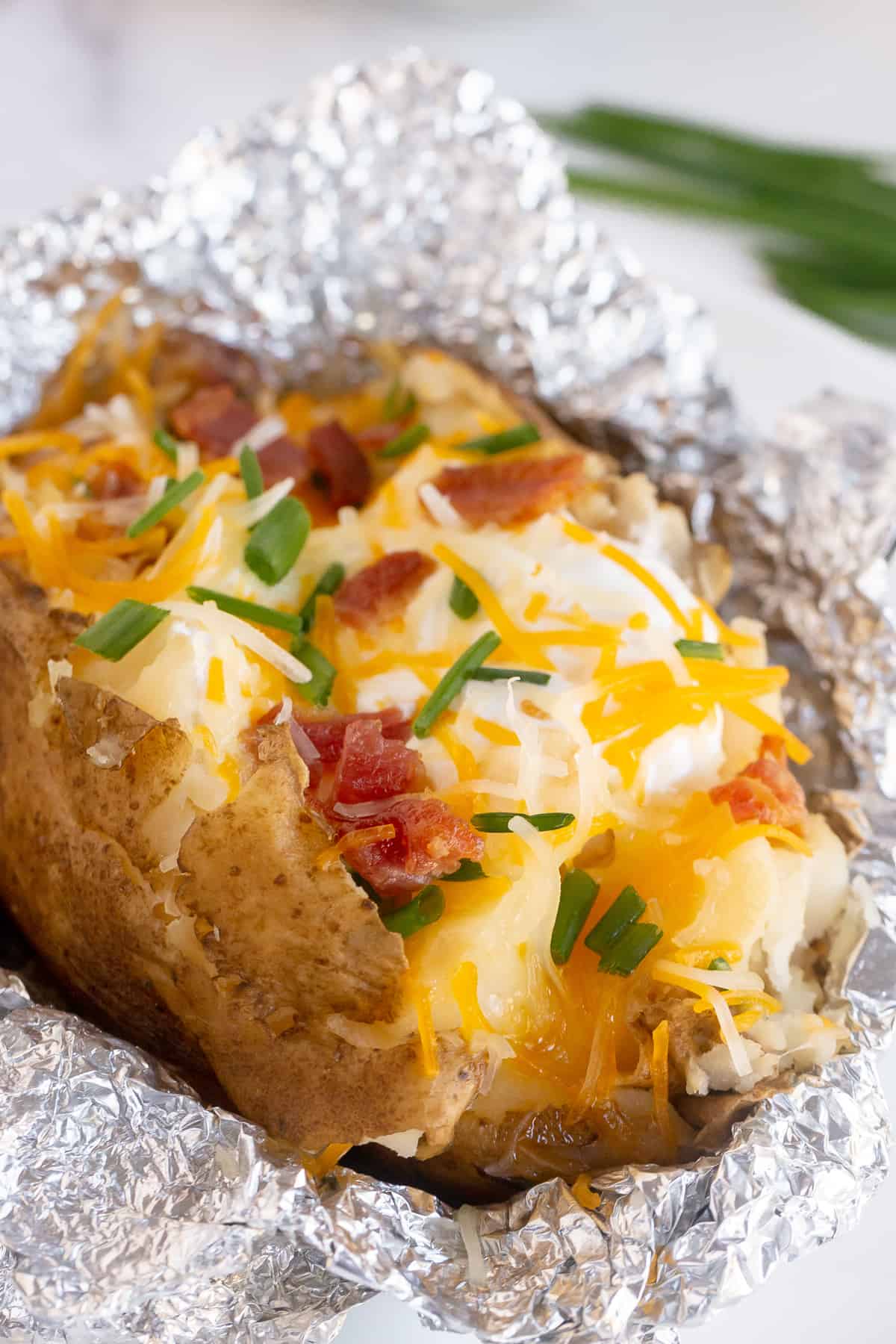A baked potato topped with cheese, sour cream, and bacon on top of foil.