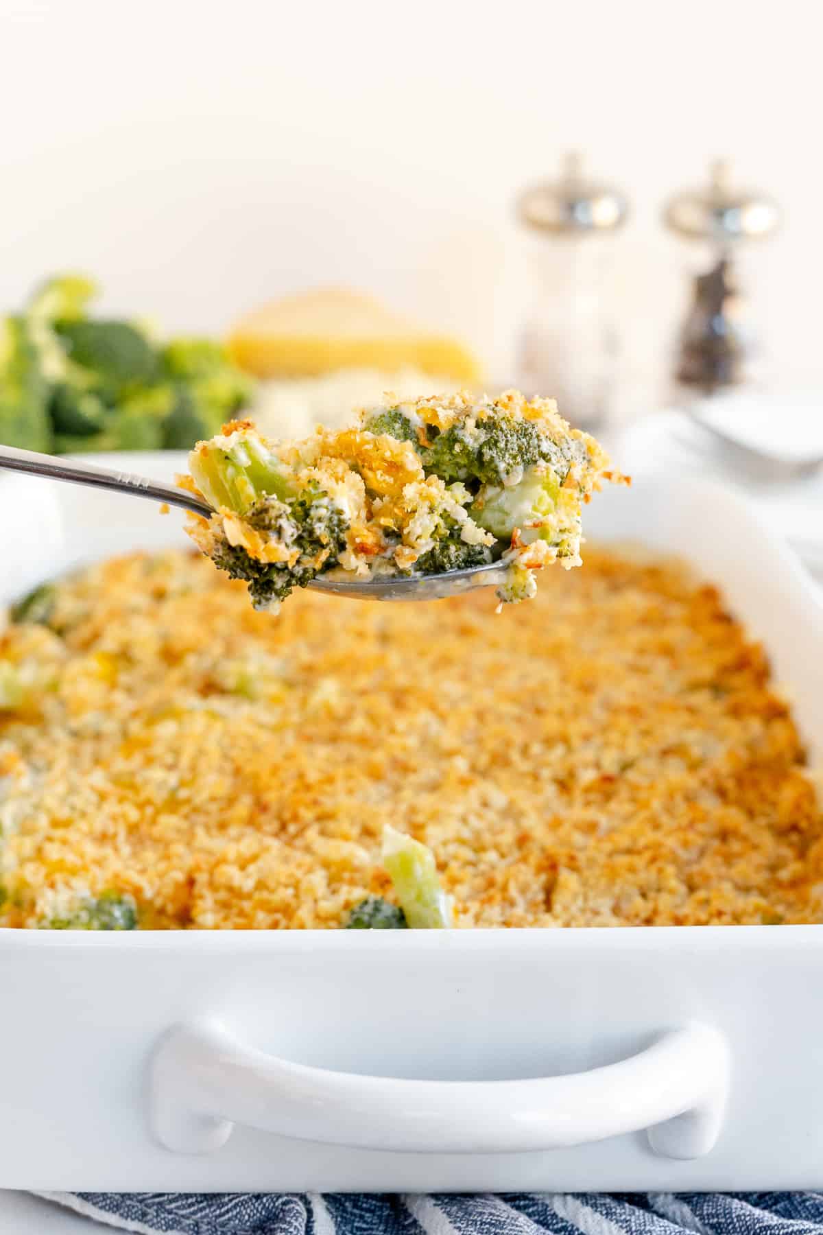 A spoon scoops up some broccoli and pearl onion casserole from a baking dish.