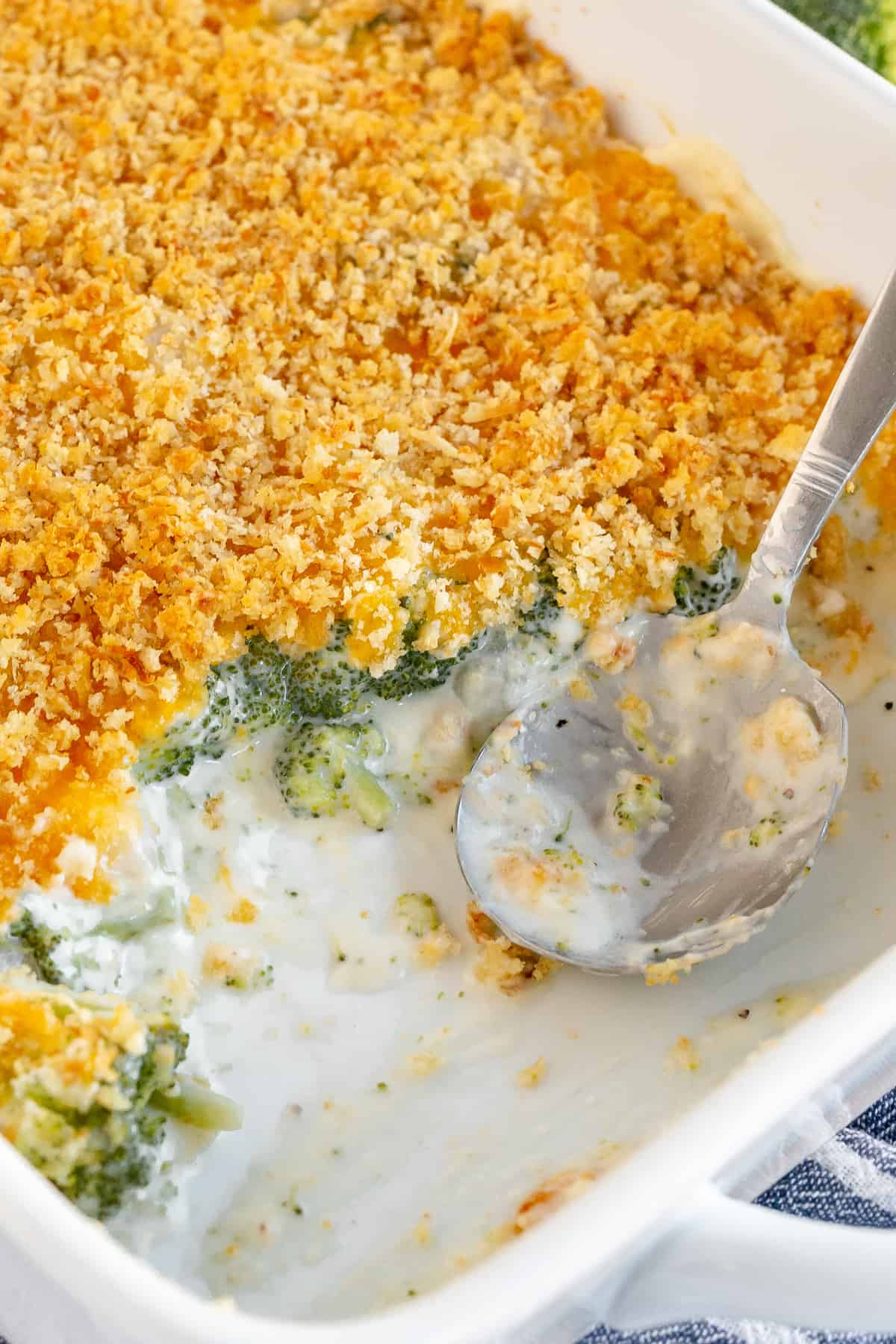 A close up of a spoon resting in a dish full of Broccoli Pearl Onion Casserole.