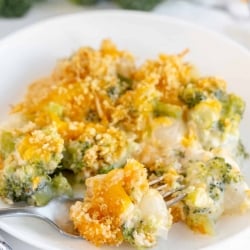 A fork breaks into a serving of Broccoli Pearl Onion Casserole on a white plate.