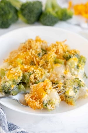 A fork breaks into a serving of Broccoli Pearl Onion Casserole on a white plate.