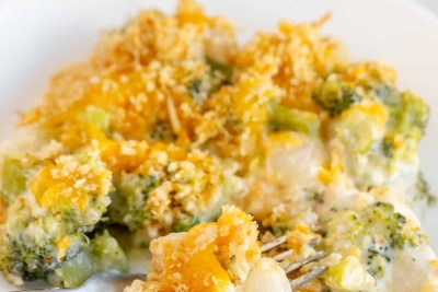 A fork breaks into a serving of Broccoli Pearl Onion Casserole on a white plate.