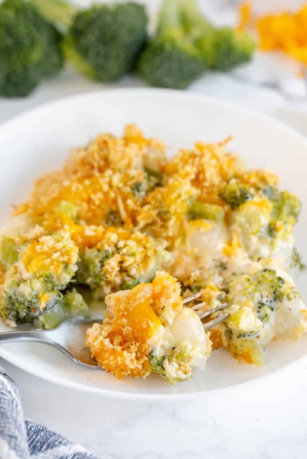 A fork breaks into a serving of Broccoli Pearl Onion Casserole on a white plate.