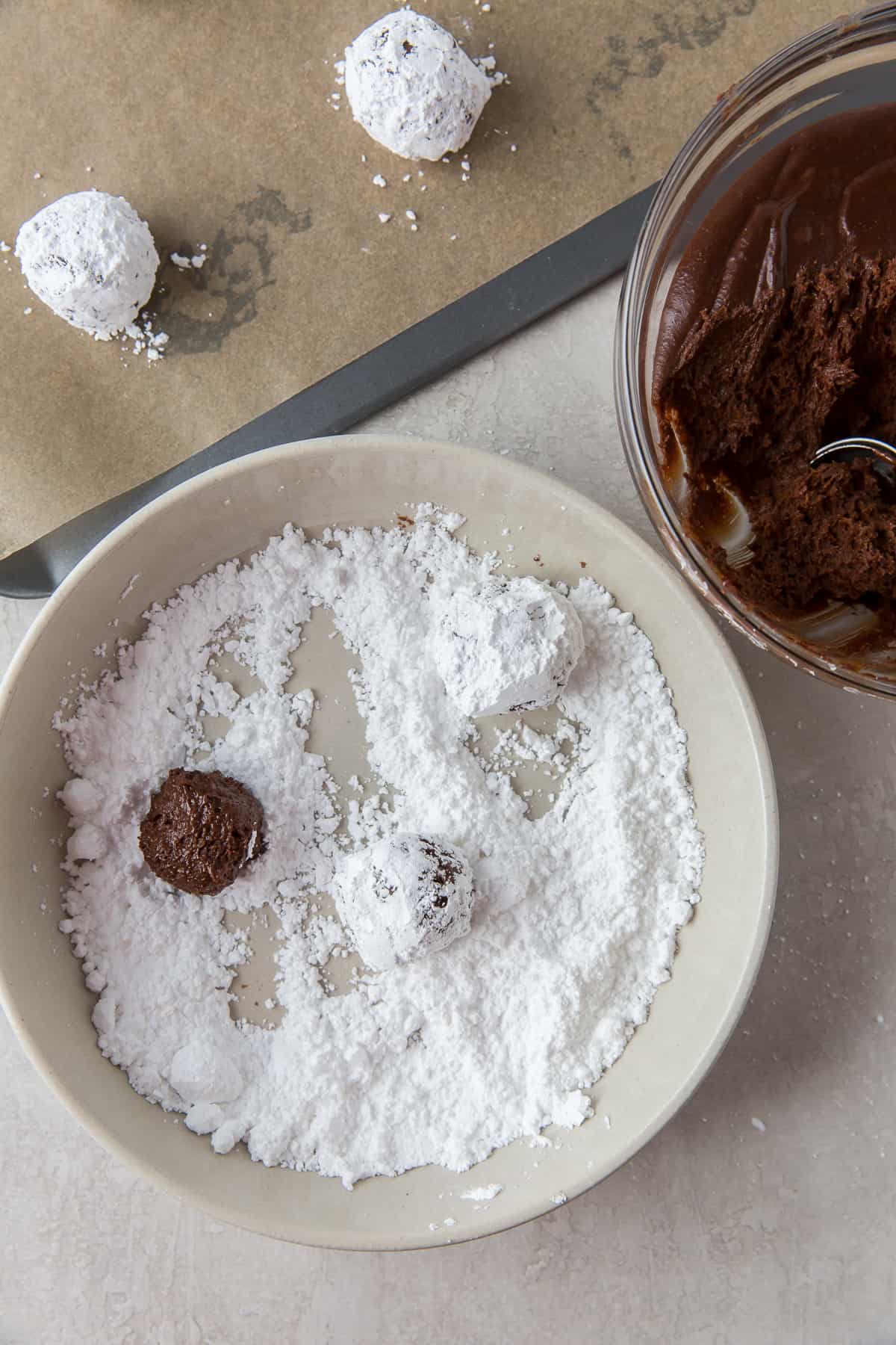 Balls of chocolate cookie dough in a bowl of powdered sugar.