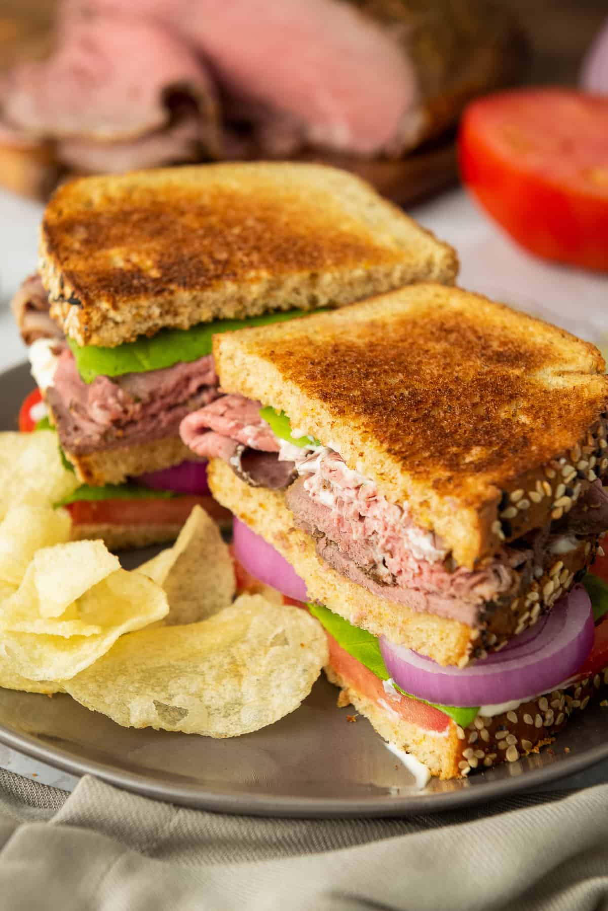 A roast beef sandwich sliced in half on a plate with chips.