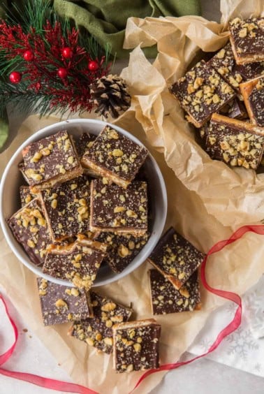 A bowl filled with Toffee Candy surrounded by red ribbon and greens.
