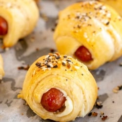 A close up of a pig in a blanket topped with everything bagel seasoning on a baking sheet.