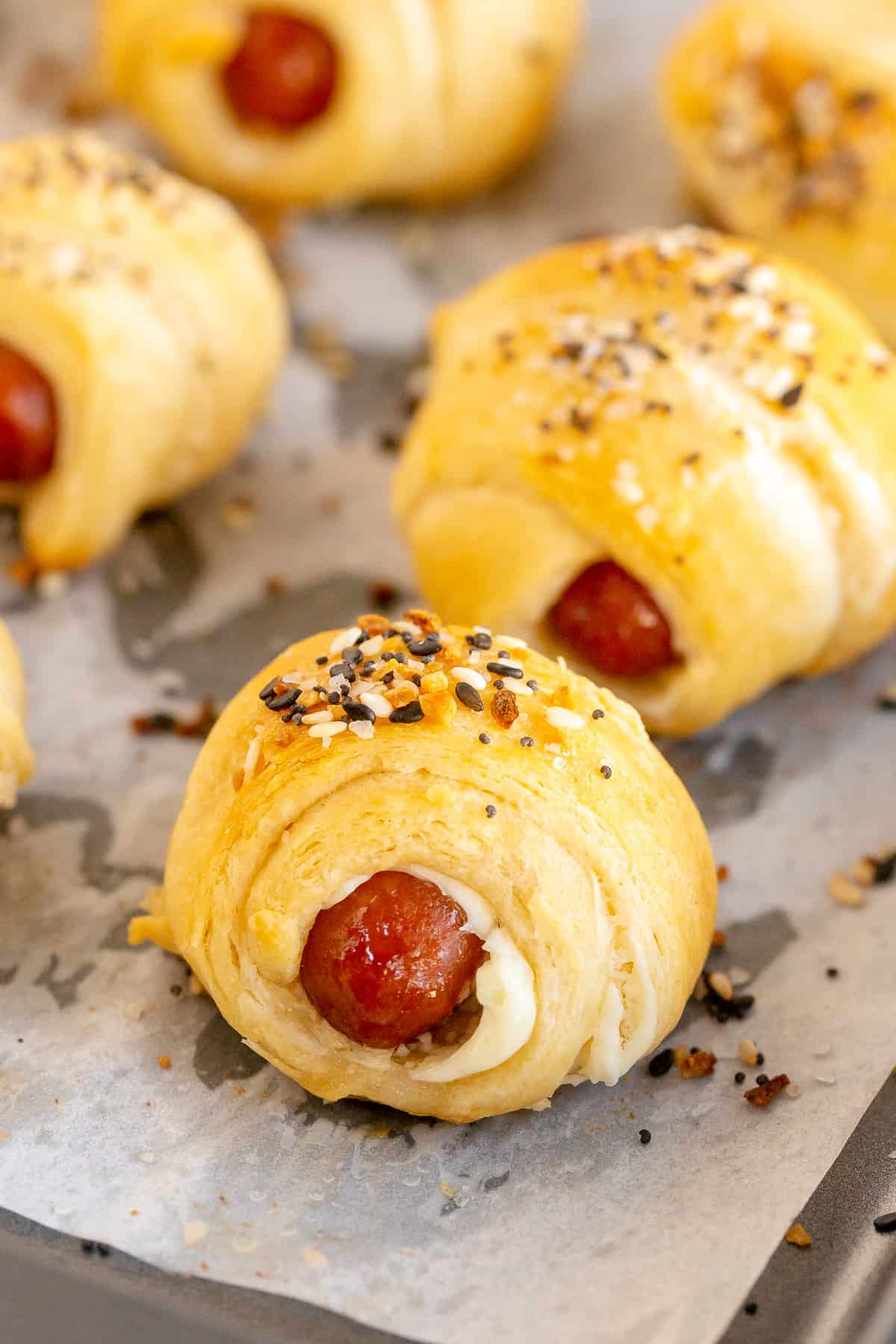 A close up of pig in a blanket topped with everything bagel seasoning on a baking sheet.