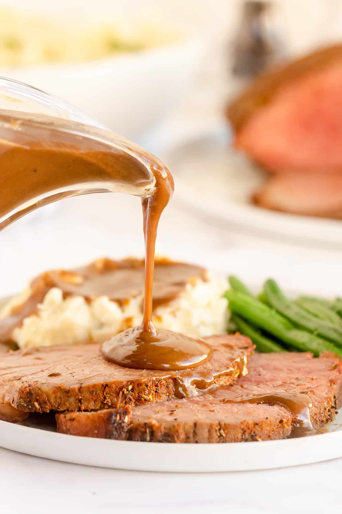 Gravy pouring on to slices of roast beef.