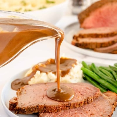 Gravy pours on to slices of roast beef.