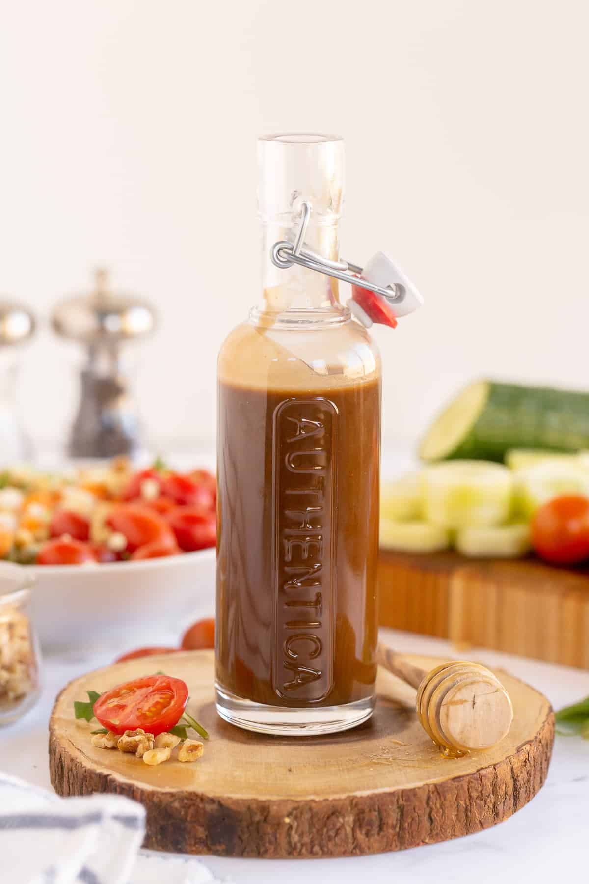 A glass container filled with salad dressing with vegetables around it.